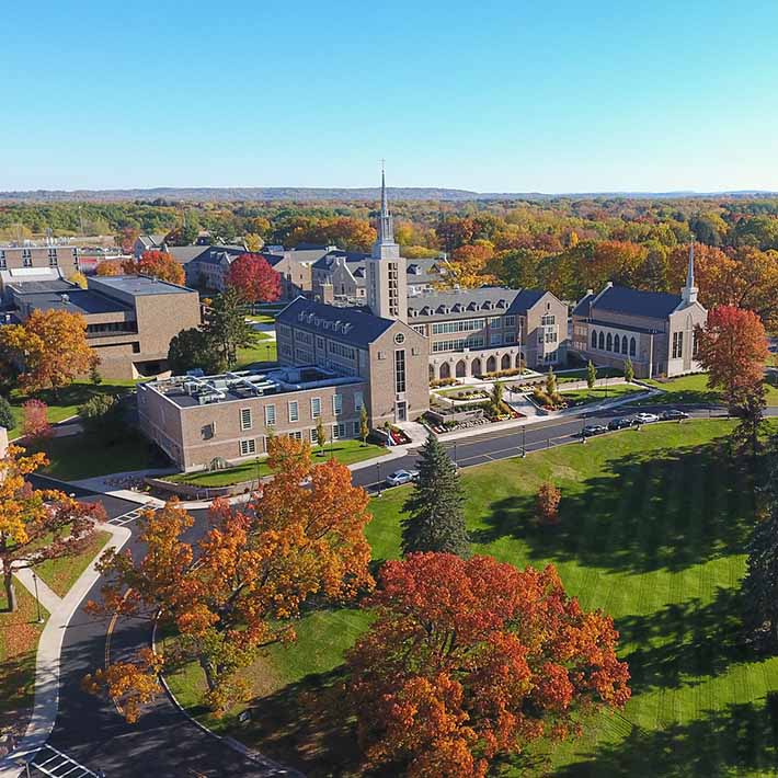 Aerial view of ϲַȫ Fisher University with colorful leaves on trees, bright green grassy hills, and sun glistening on buildings.